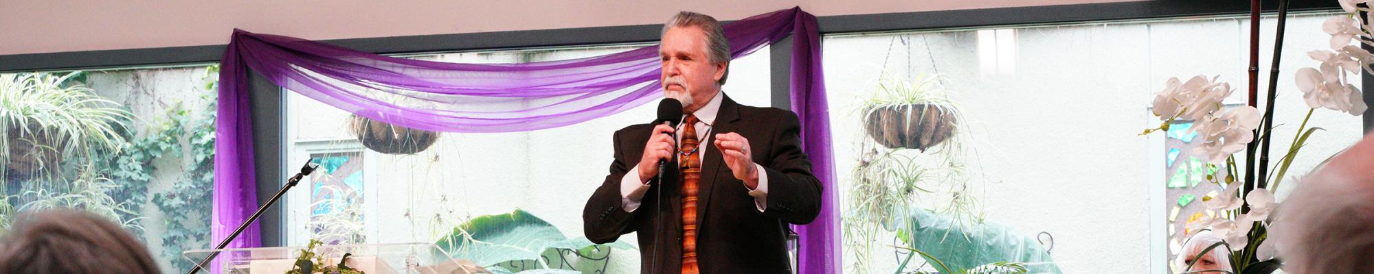 Image is Rev. Greg Dorst speaking at the front of the sanctuary.